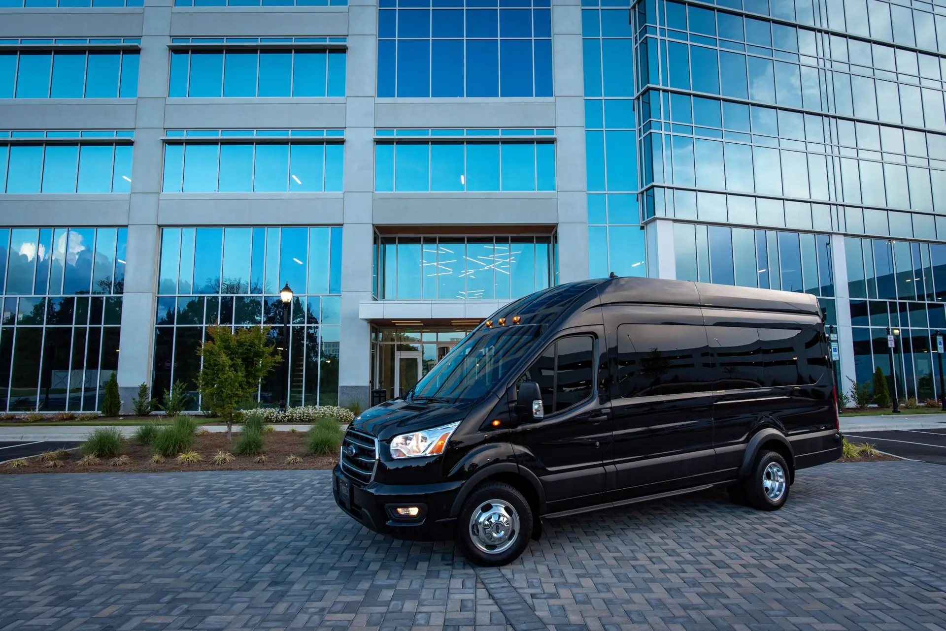 Black luxury van parked in front of a modern office building under daylight.